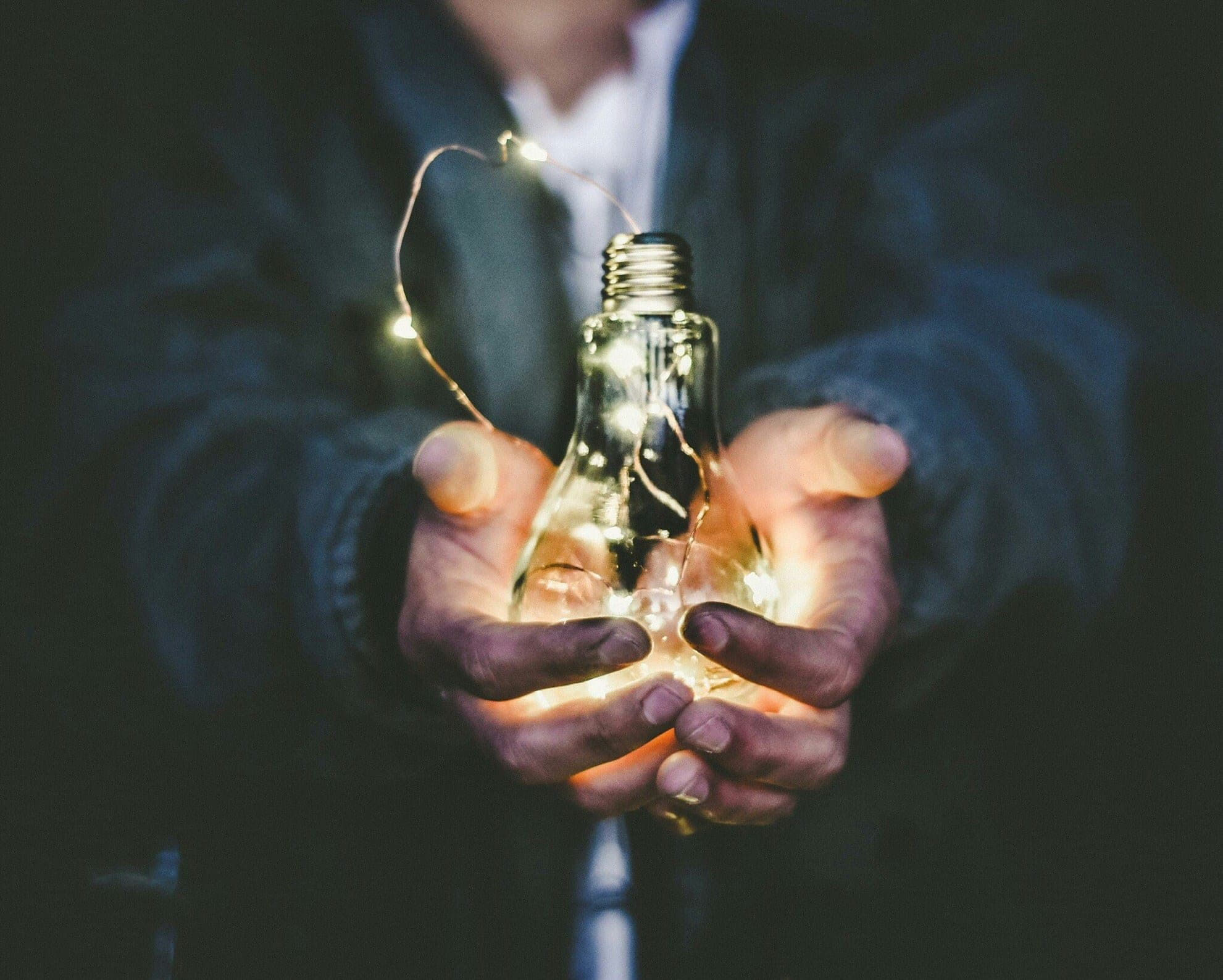 A pair of hands cupping a lit bulb in the dark